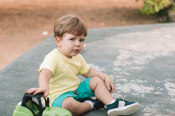 A young boy sitting outdoors on a warm day, enjoying playtime with a toy.